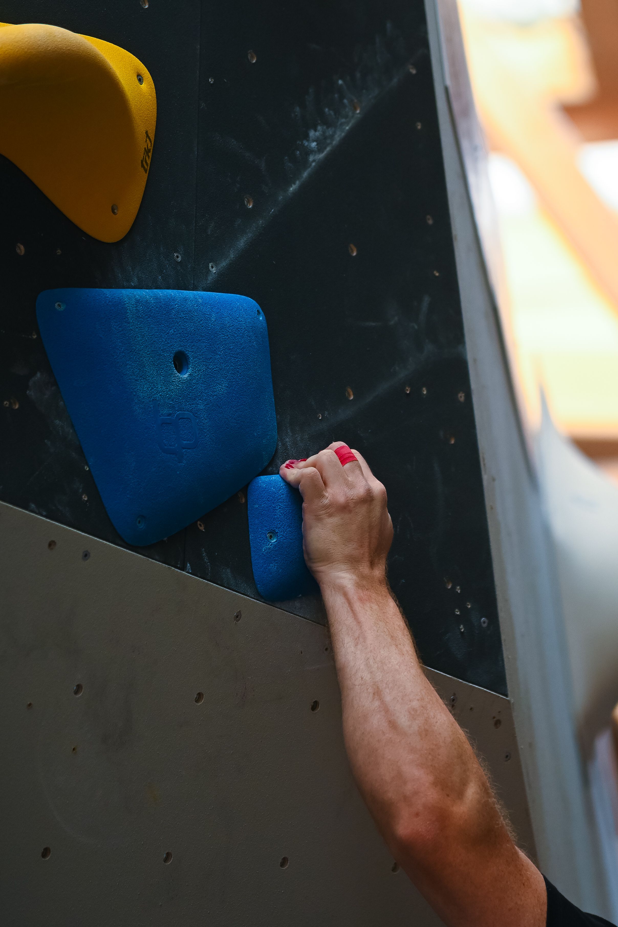 A climber's hand grips a blue climbing hold on an indoor bou