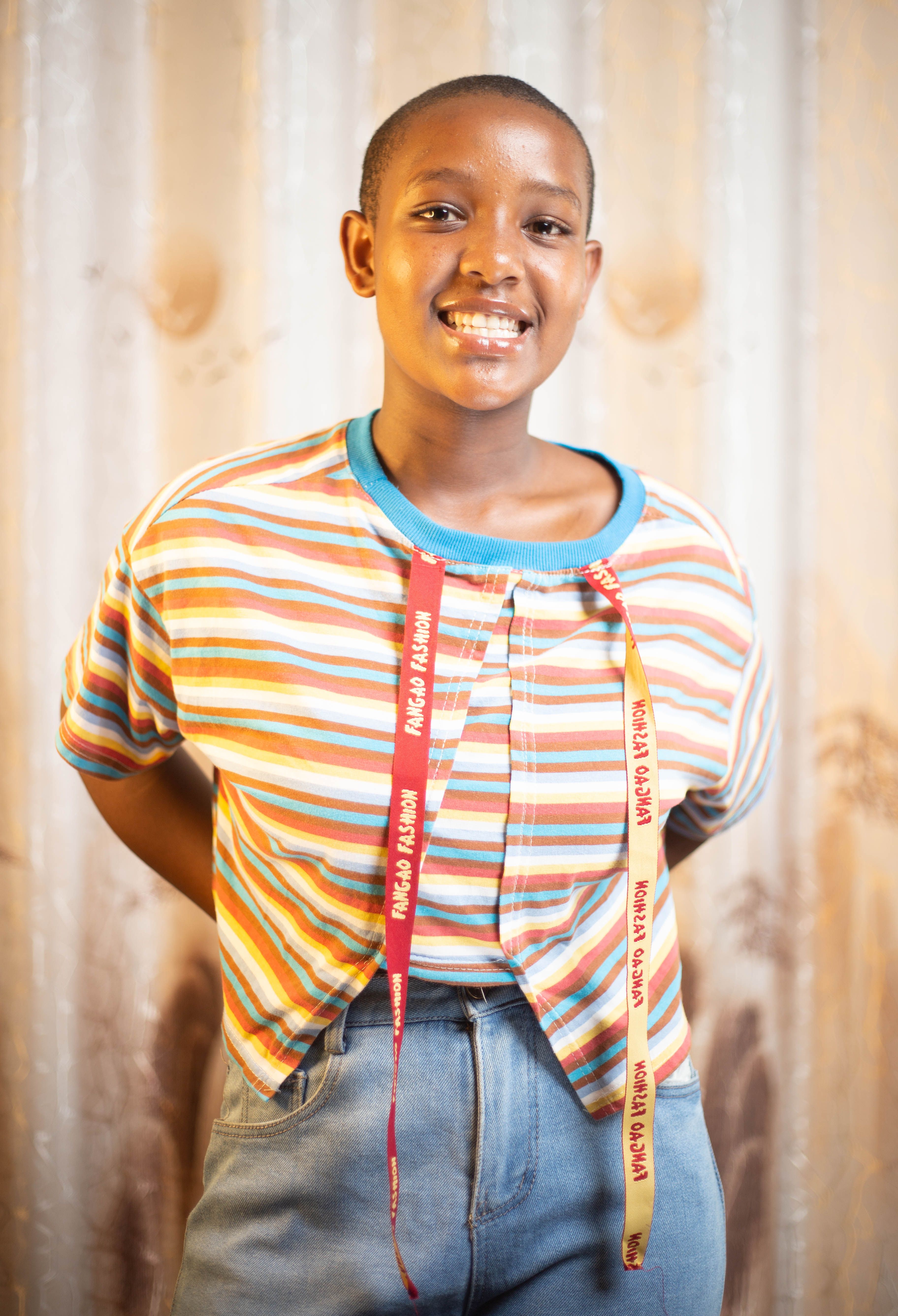 Smiling young adult standing indoors wearing a bright striped shirt and lanyards.
