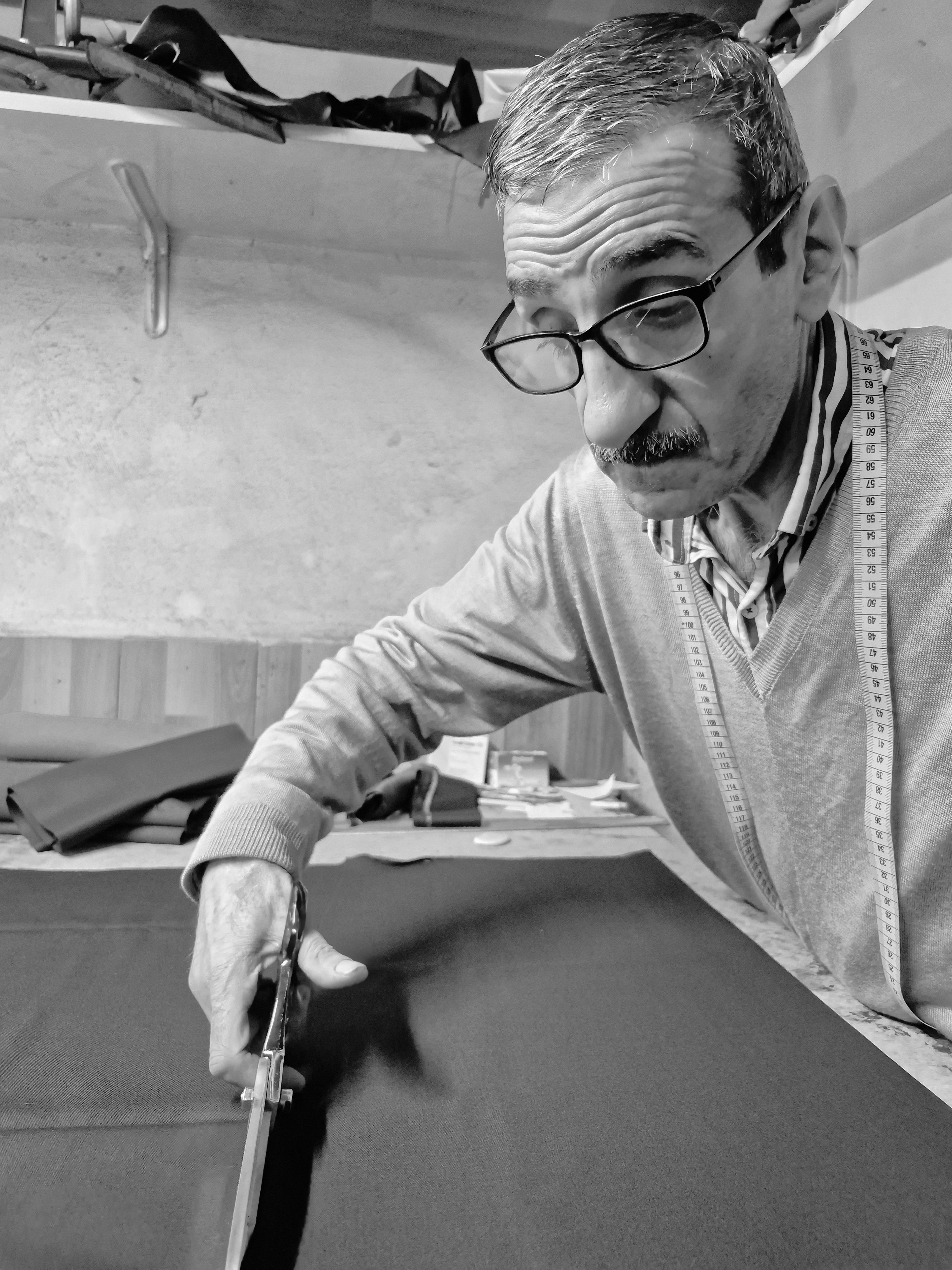 Focused tailor skillfully cutting fabric with scissors in a workshop setting.