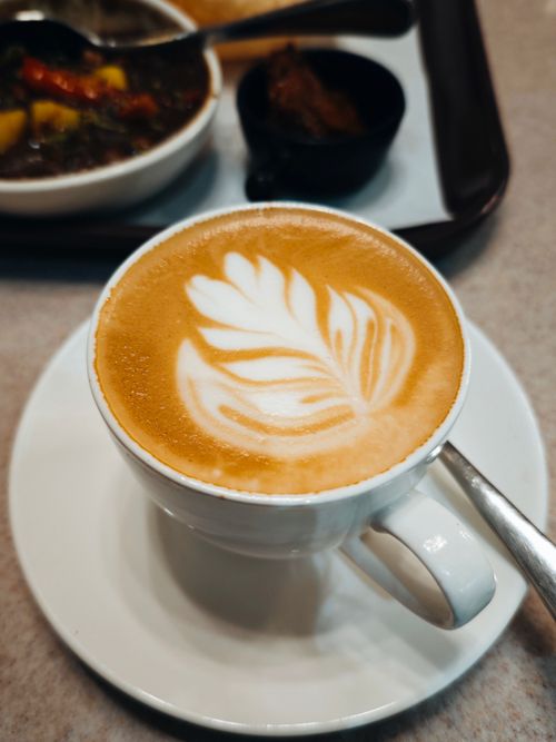 Free A close-up shot of a coffee cup with intricate leaf latte art, perfect for cafe themes. Stock Photo