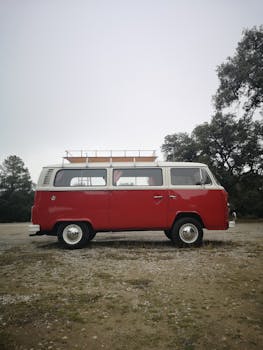 Side view of a vintage red Volkswagen Kombi parked outdoors on a cloudy day.