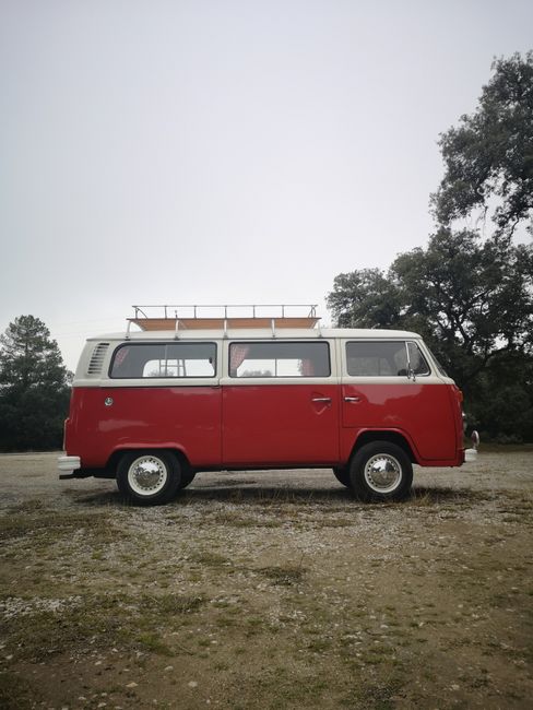 Side view of a vintage red Volkswagen Kombi parked outdoors on a cloudy day.