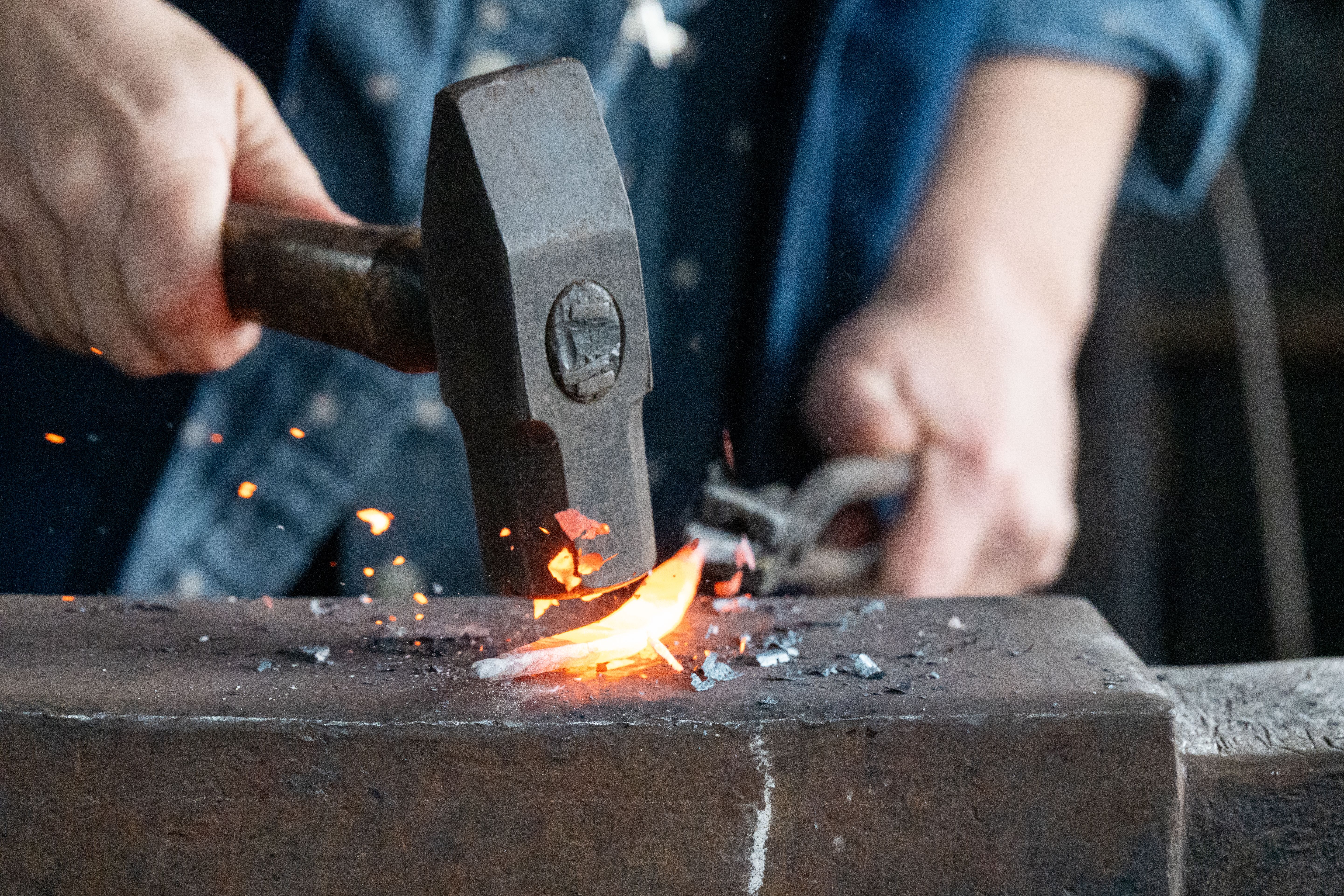 Blacksmith forging glowing metal on anvil with hammer in a traditional workshop setting.