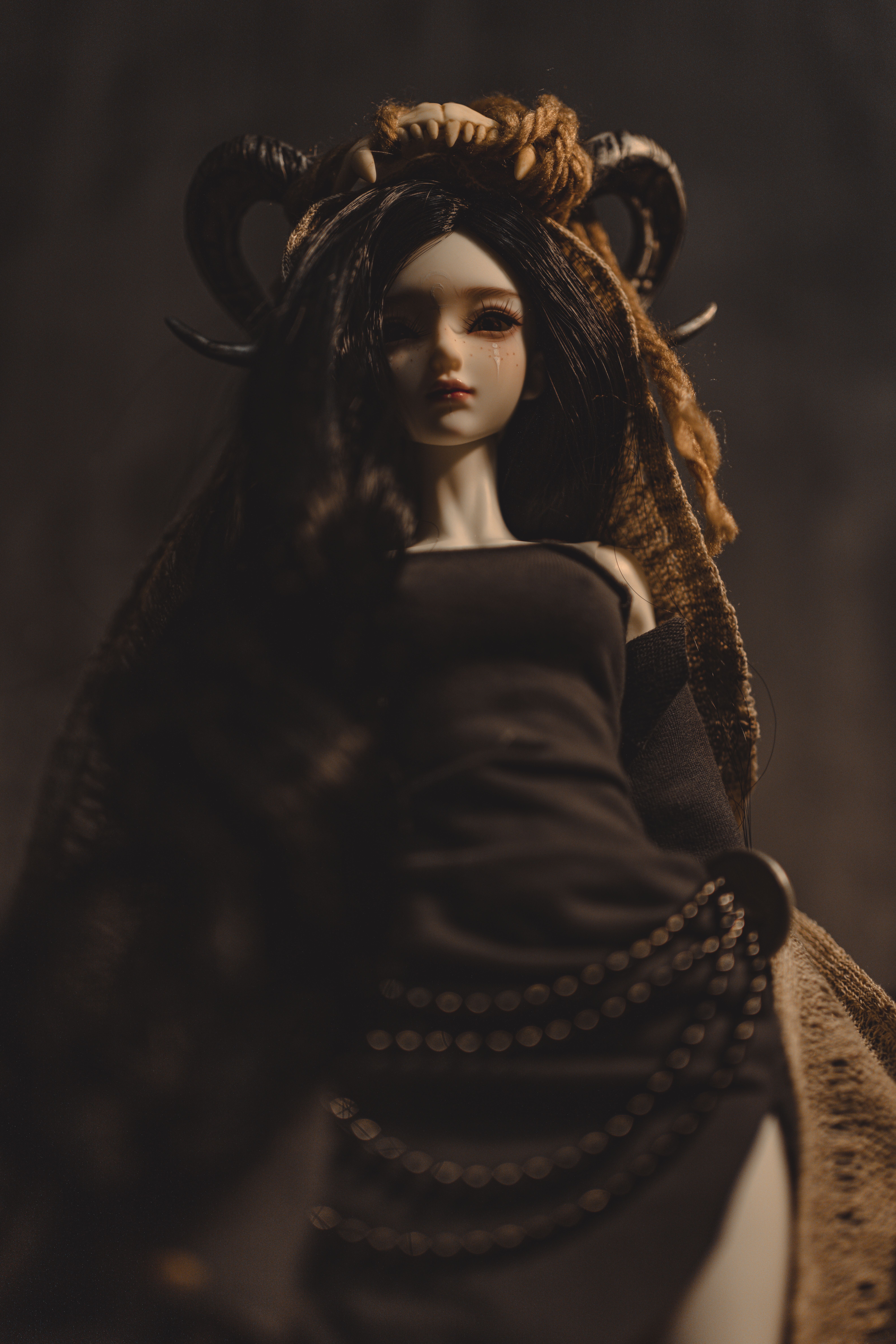 Gothic doll with intricate horns, wearing a black dress in a moody, dark atmosphere.