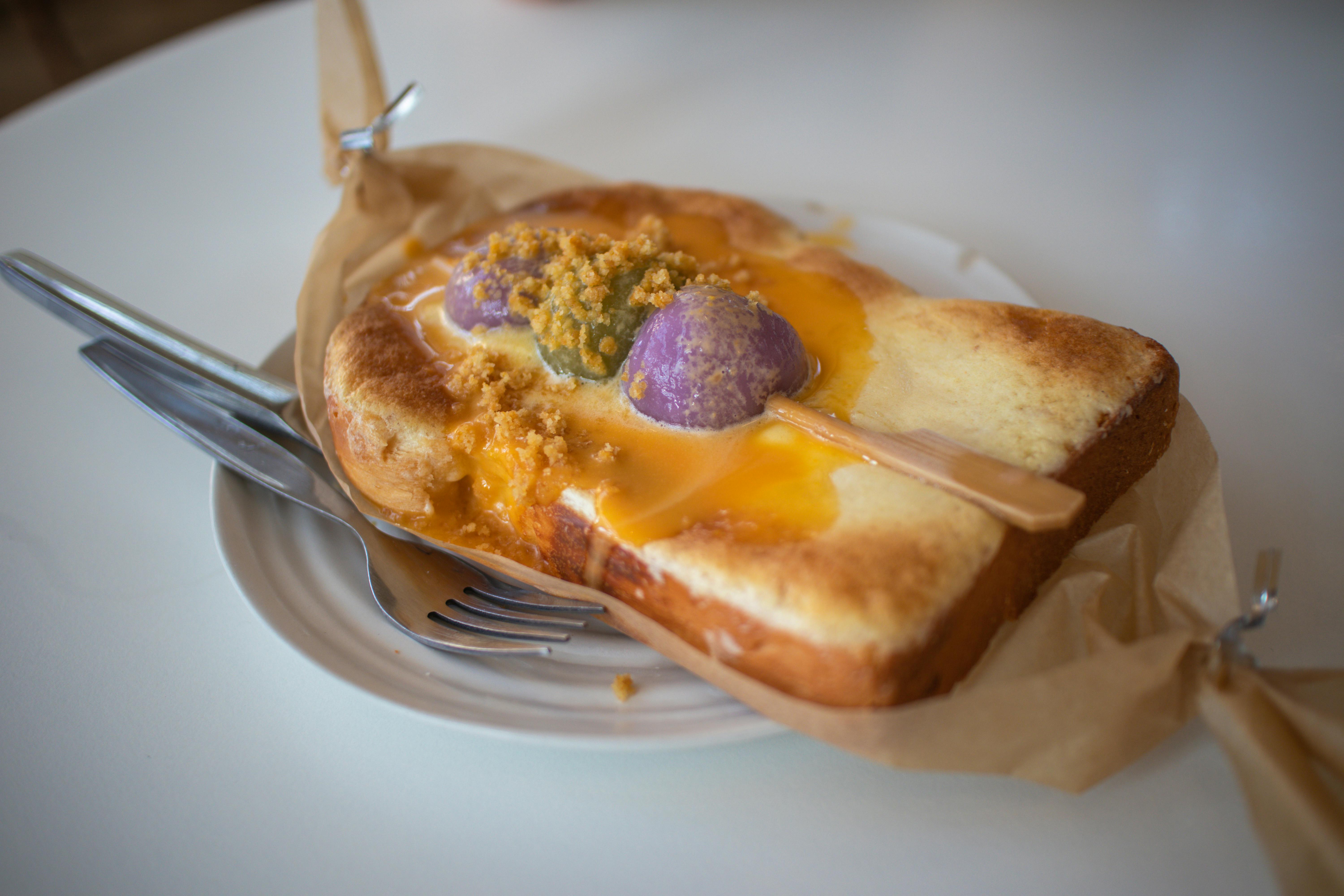 Close-up of a sweet toast topped with vibrant spreads and crumbles, served on a white plate.