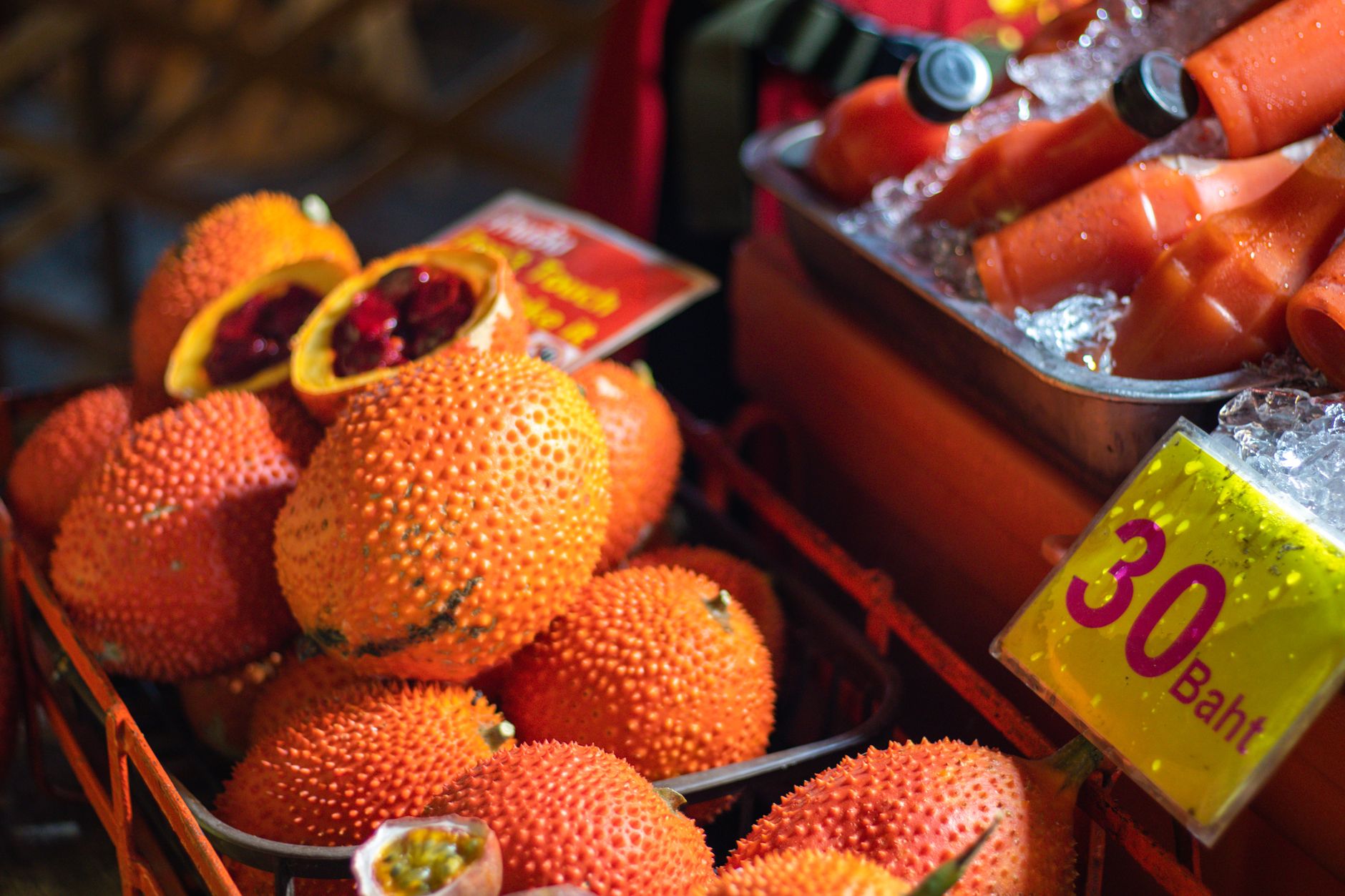 Vivid display of exotic gac fruits and fresh juice bottles at a night market stall.