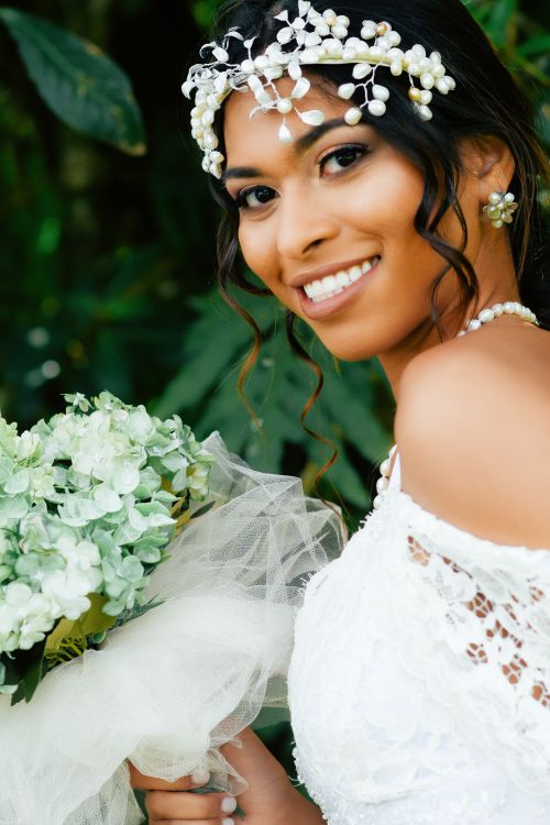Free A smiling bride holding a bouquet with lush greenery in the background, showcasing elegance and joy. Stock Photo