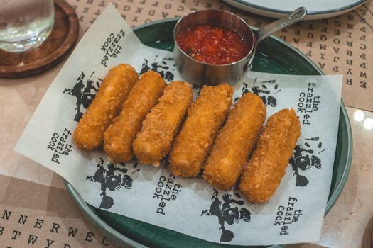 Golden-brown mozzarella sticks served with marinara sauce on a restaurant table.