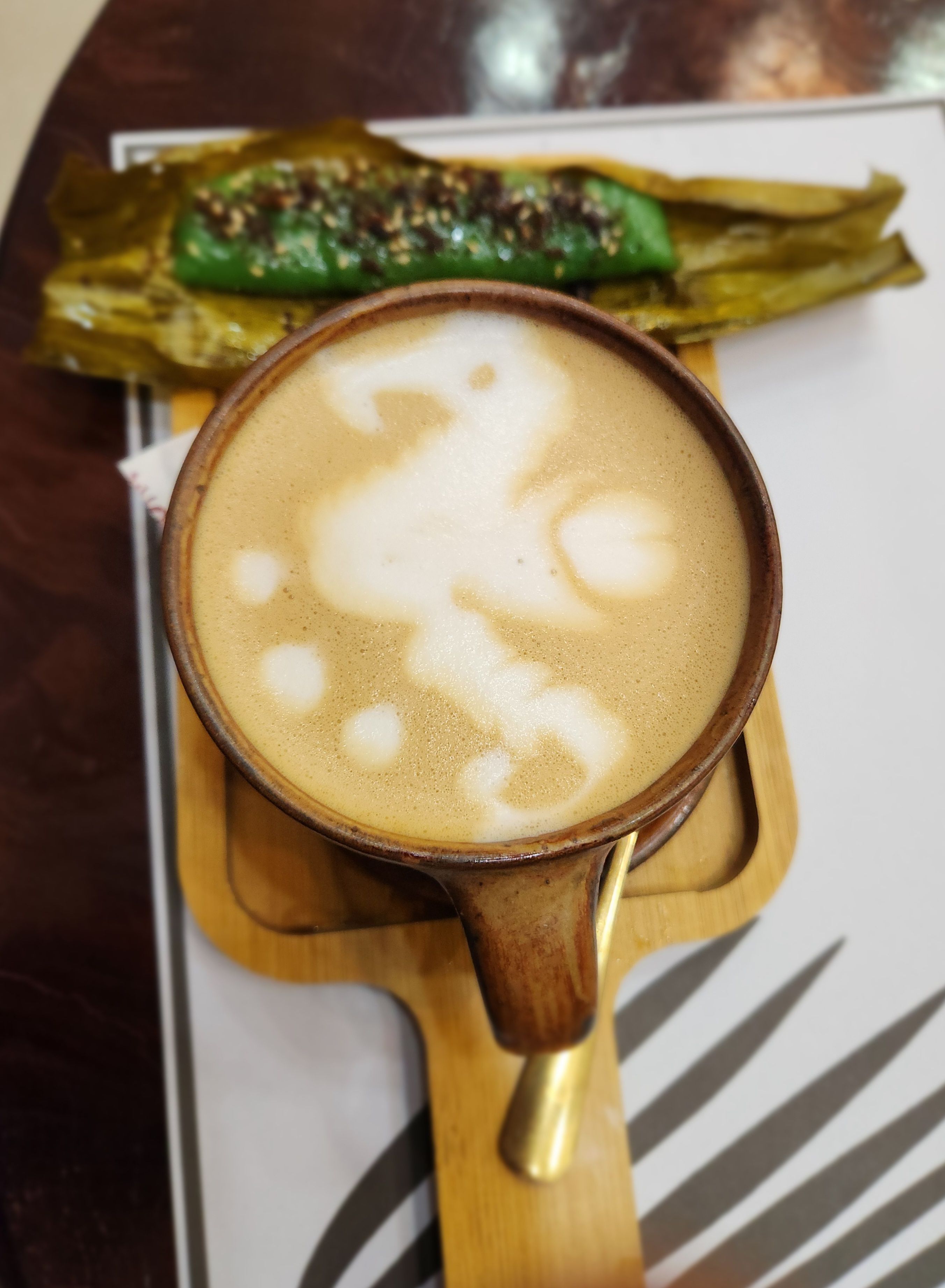 A beautifully crafted latte art with a side of traditional Filipino dessert suman on a wooden tray.