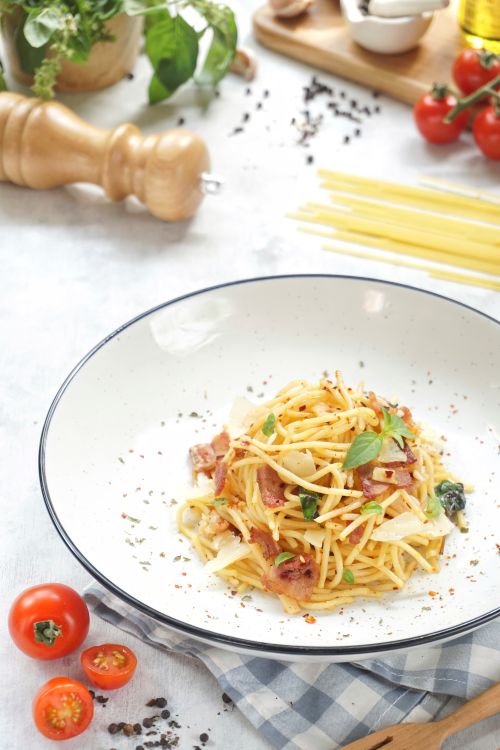 Free A plate of spaghetti carbonara garnished with basil and served with fresh tomatoes and herbs. Stock Photo