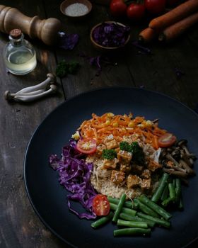Vibrant vegan Buddha bowl featuring fresh vegetables, tempeh, and grains on a dark rustic table.