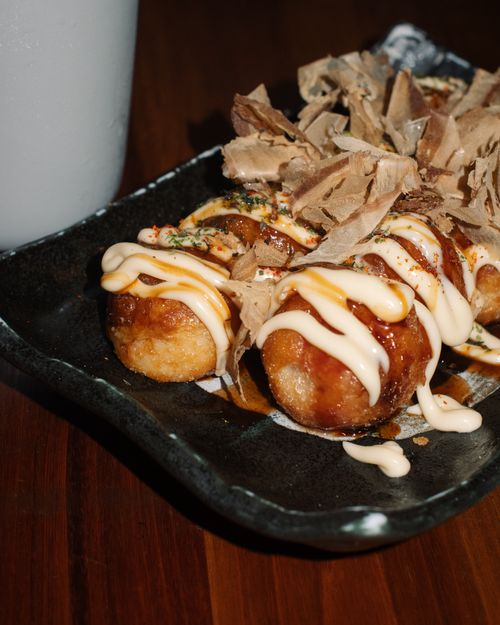 Free Close-up of takoyaki balls garnished with mayonnaise and truffle flakes on a black plate. Stock Photo