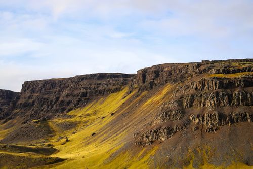 Free A breathtaking view of a sunlit cliff face on an island, showcasing dramatic rock formations and lush greenery. Stock Photo