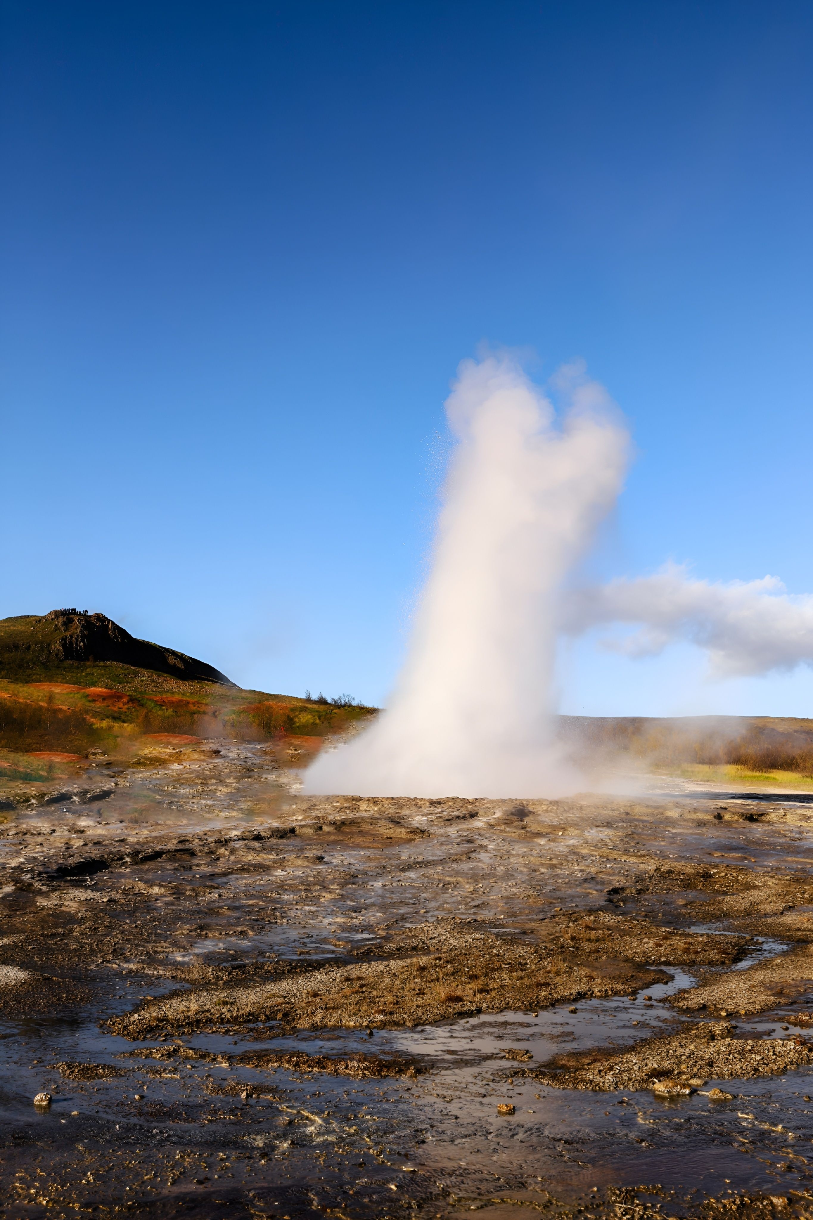 A dramatic geyser erupts on a remote island under a clear blue sky.