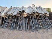 A collection of closed beach umbrellas stacked upright on a sandy beach with a clear blue sky.