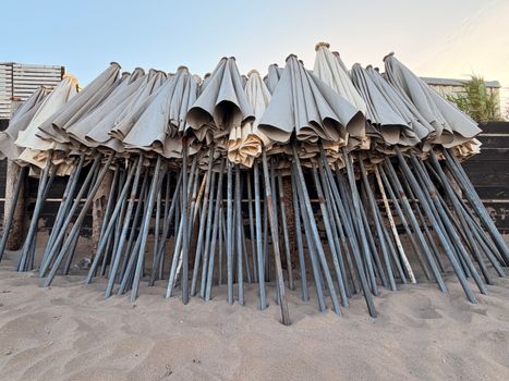 A collection of closed beach umbrellas stacked upright on a sandy beach with a clear blue sky.