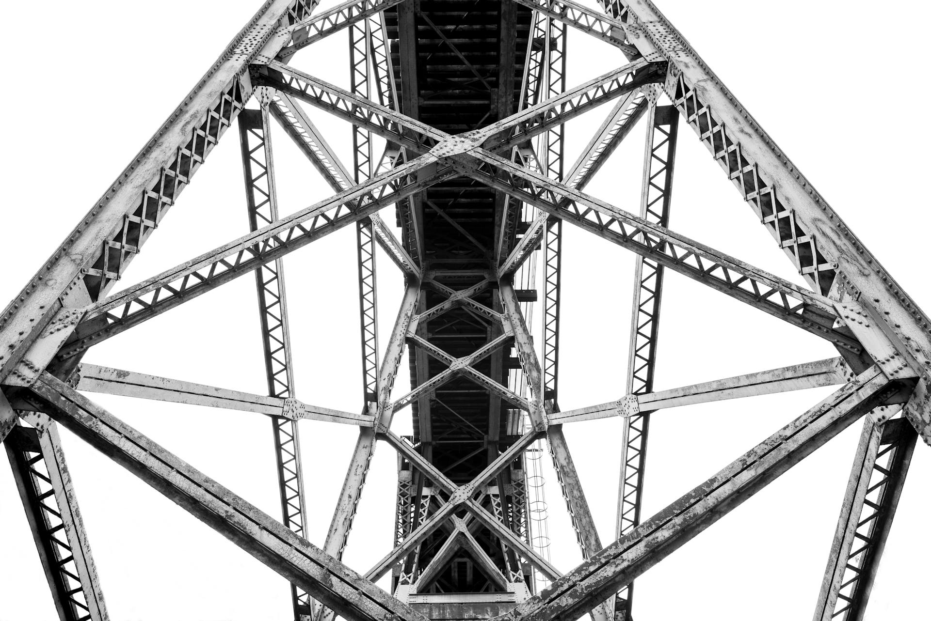 A dramatic low angle view of a steel truss bridge showing its intricate architectural framework.