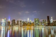 纽约市的天际线在夜间被照亮，壮丽的景色倒映在河中