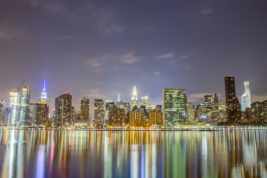 纽约市的天际线在夜间被照亮，壮丽的景色倒映在河中