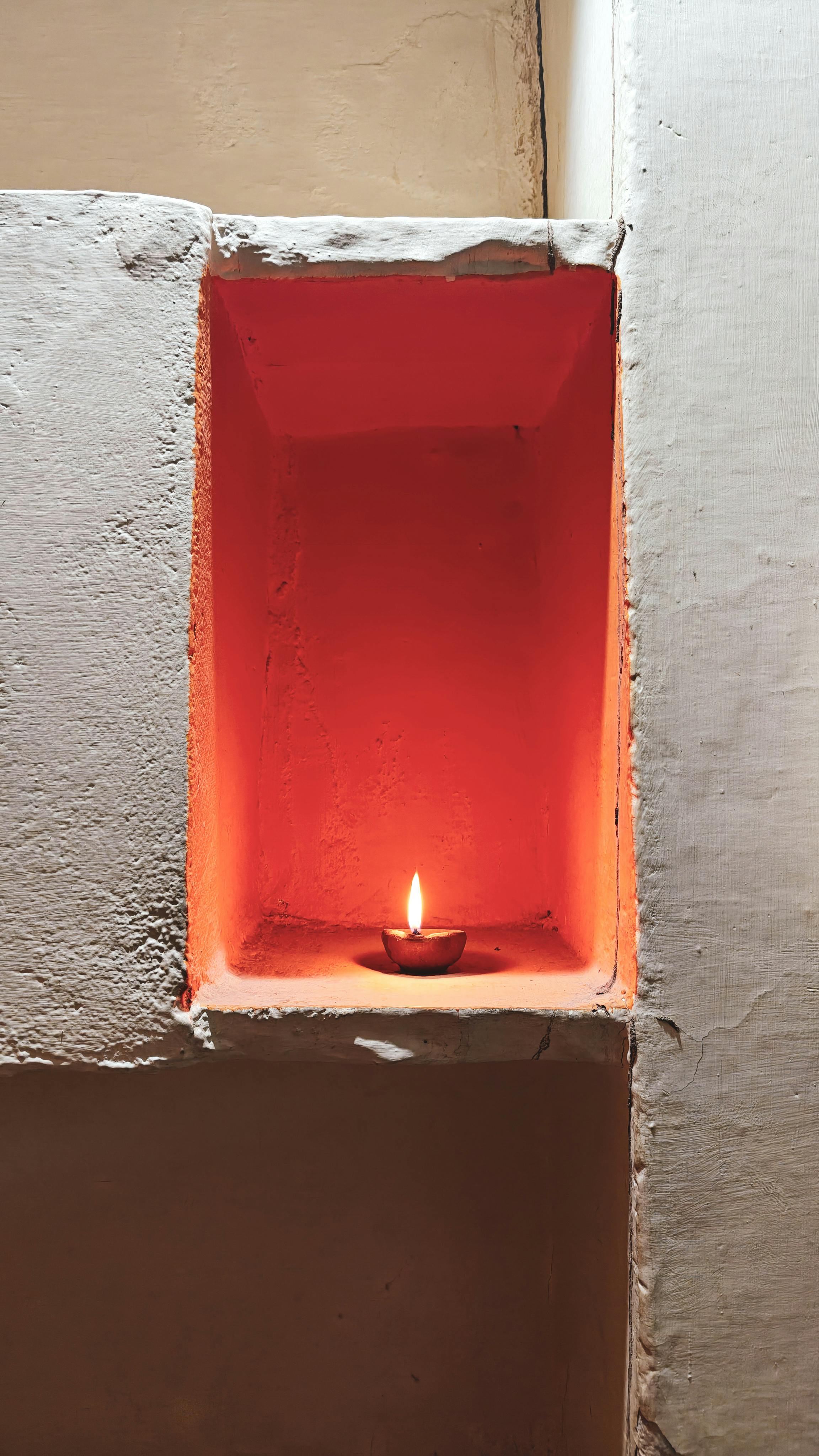 A single earthen lamp illuminating a vibrant red alcove, creating a warm and serene atmosphere.