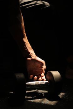 Close-up of a hand lifting a dumbbell with dramatic lighting in a gym setting.
