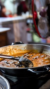 Delicious curry being prepared in a large pot at a bustling street market.