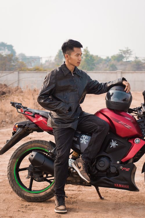Free A young man in a leather jacket poses with a red motorcycle on a sunny day in Myawaddy, Myanmar. Stock Photo