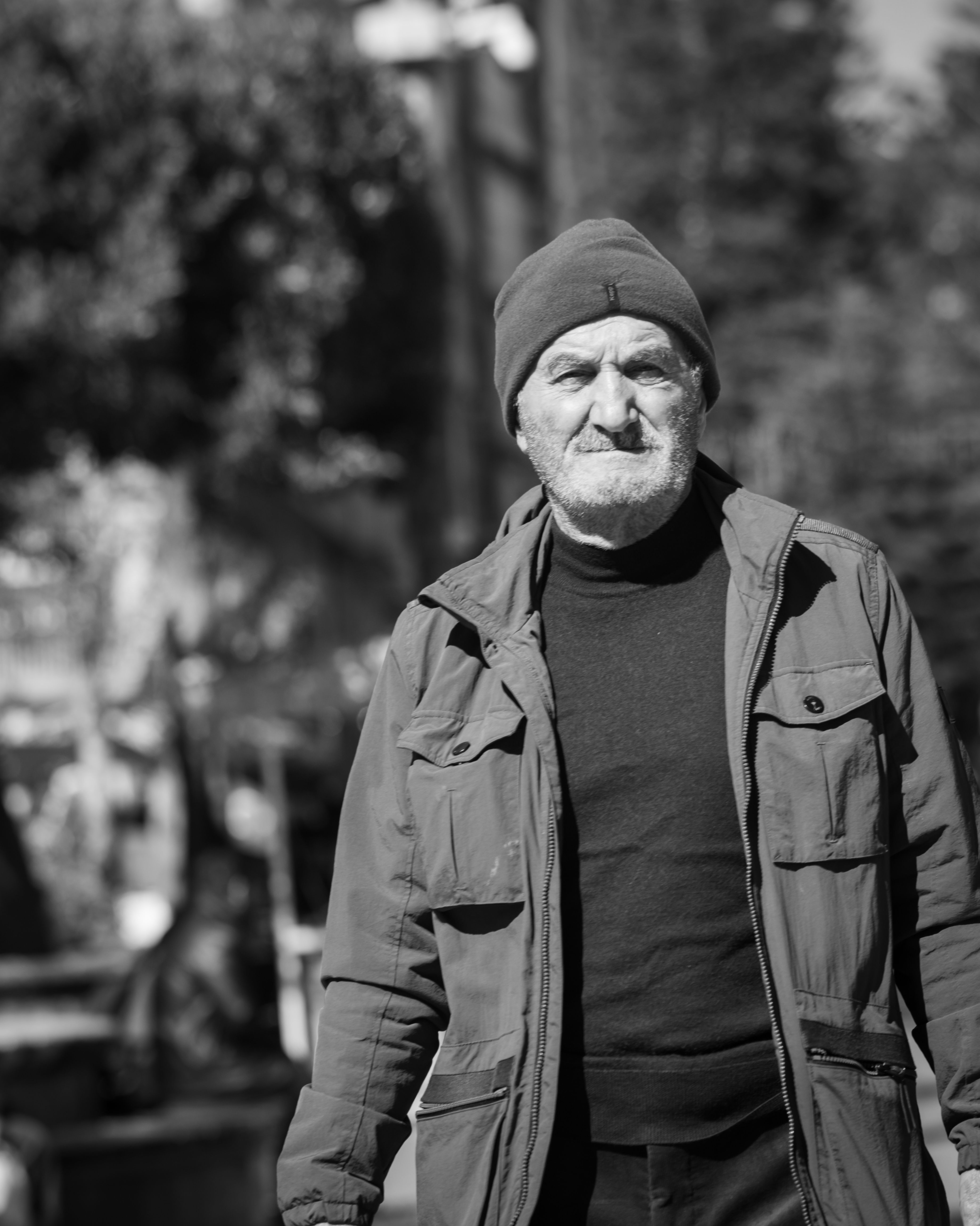 Black and white portrait of a senior man wearing a beanie outdoors.