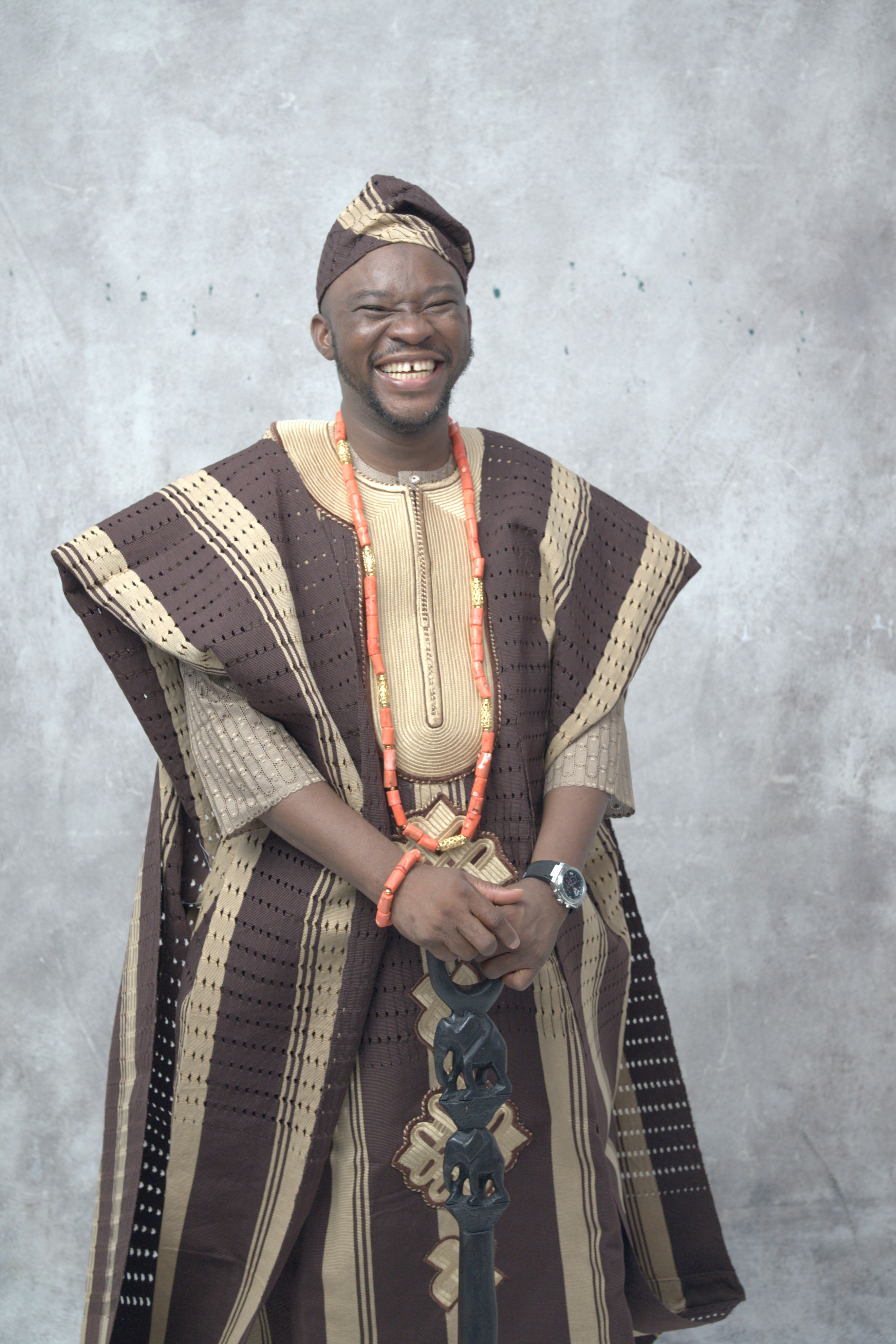 Portrait of an adult Nigerian man smiling in traditional attire with coral beads indoors.