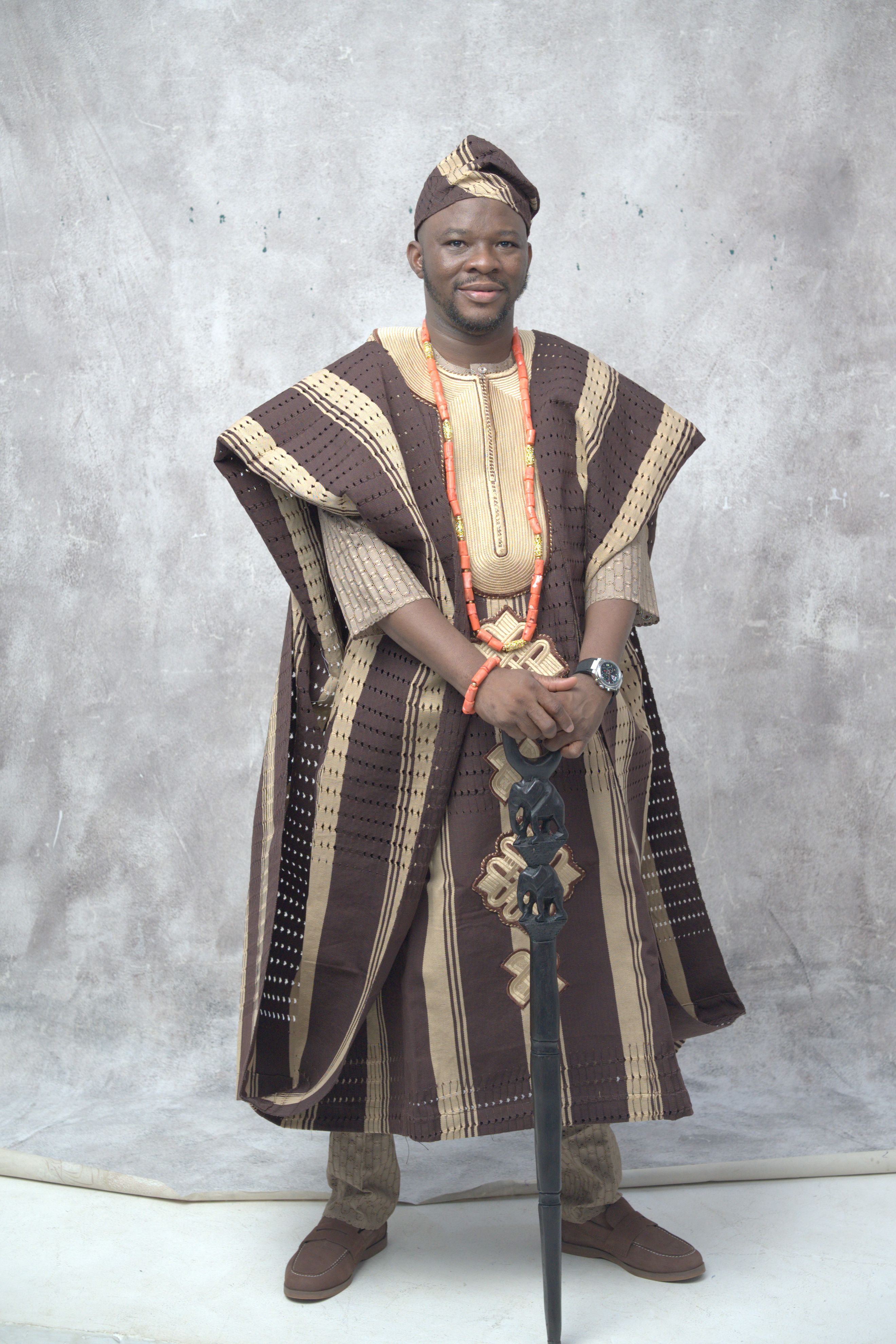 Adult man wearing traditional Nigerian Agbada with beads, standing indoors.