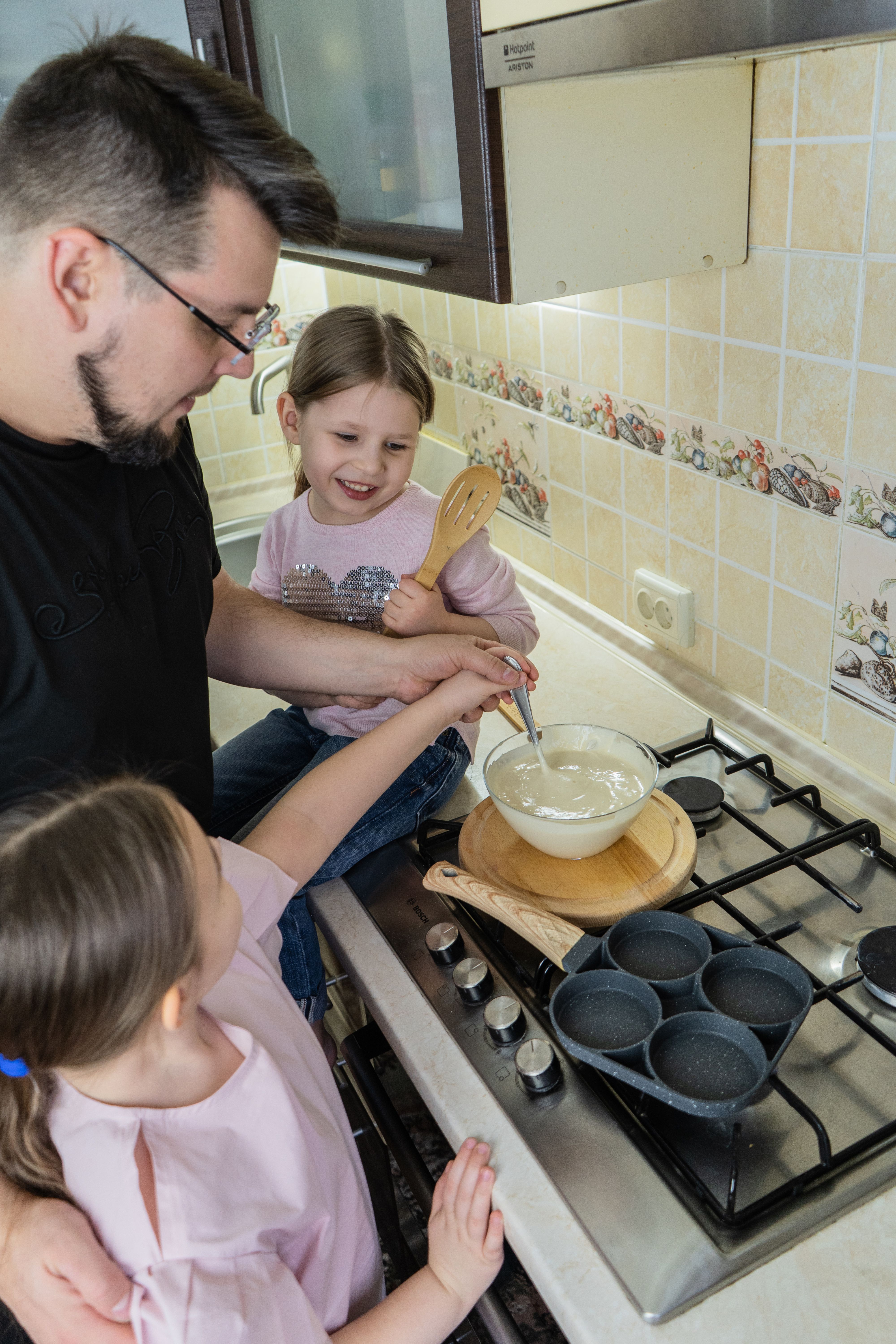 Father enjoying cooking pancakes with daughters in the kitchen.
