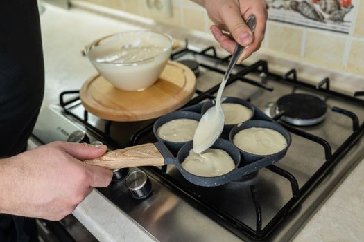 Close-up of a person preparing pancakes on a stovetop using a ladle and batter-filled skillet.