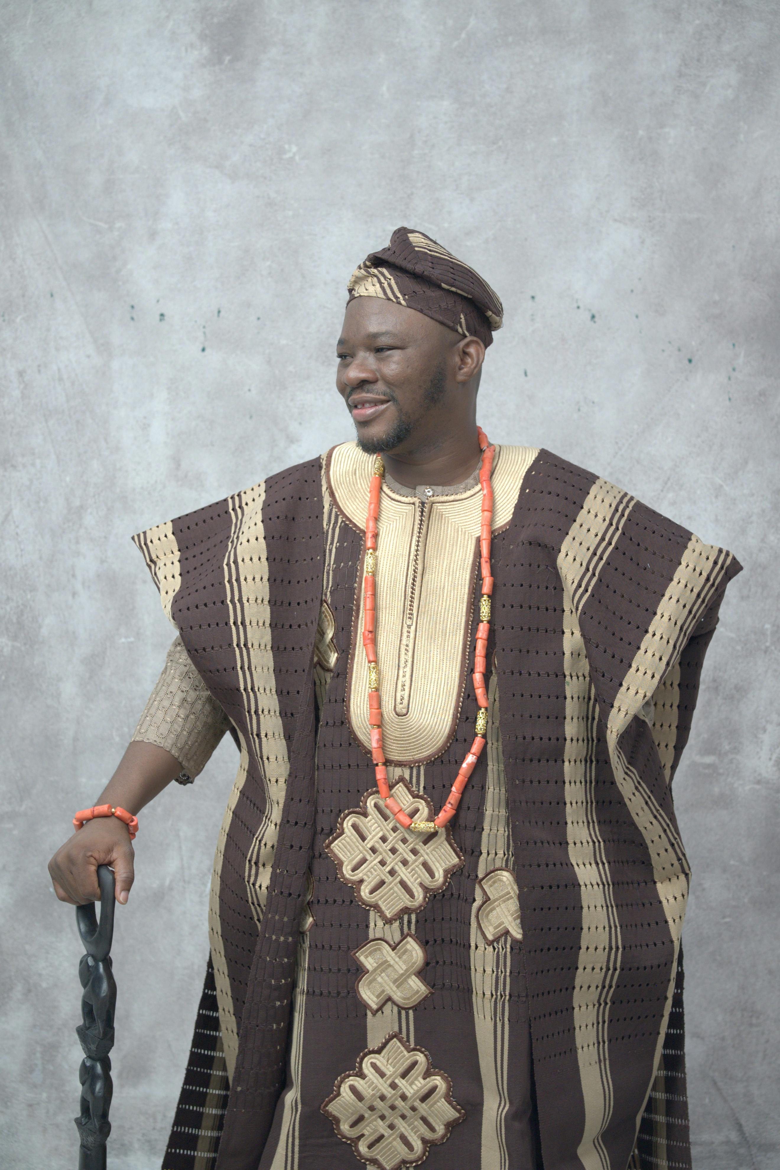 Portrait of an African man wearing traditional attire, holding a carved staff, and adorned with beaded necklaces.