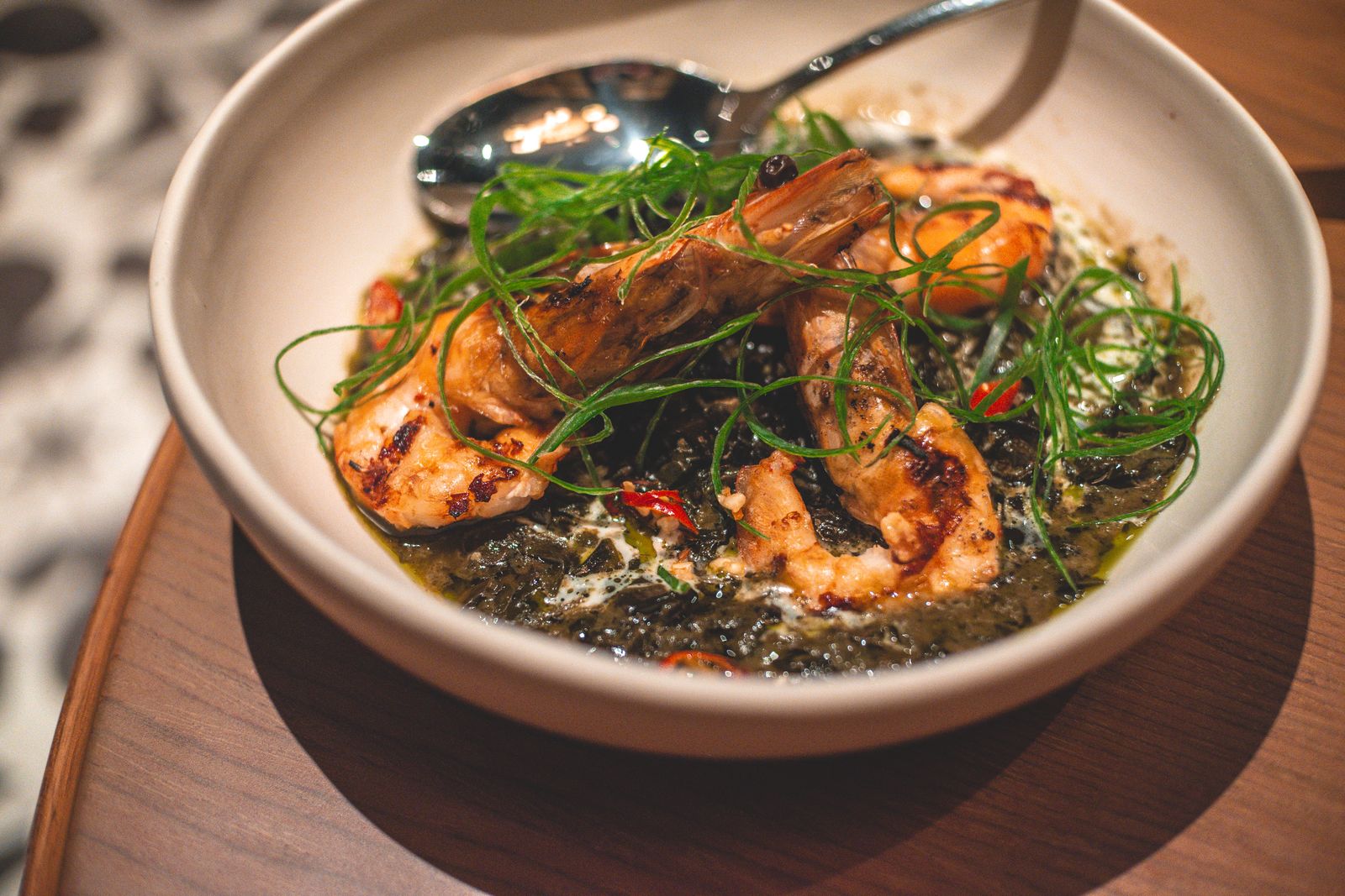 A bowl of grilled shrimp with seaweed and fresh herbs, served indoors.