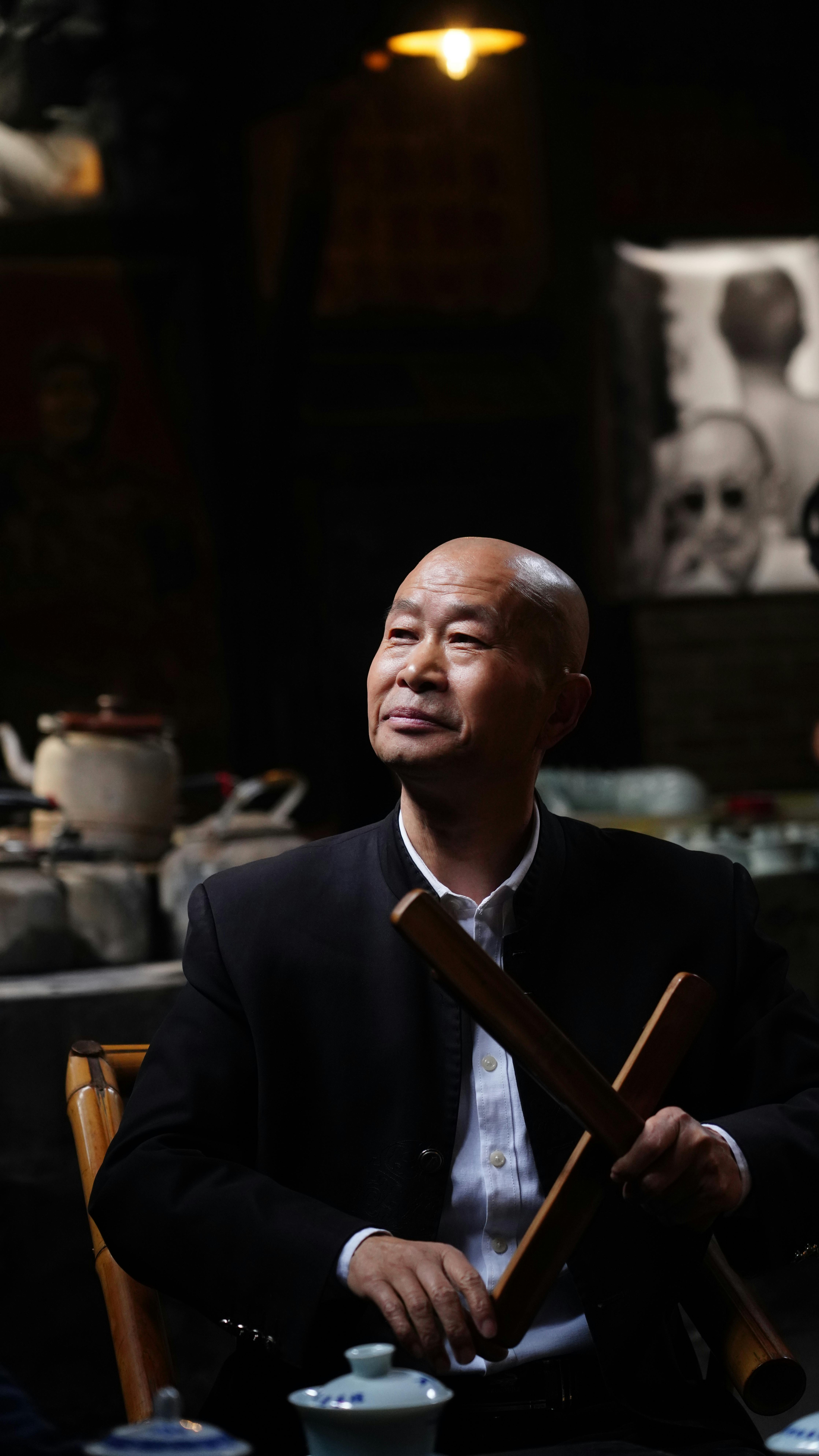 An elderly man holding instruments in a classic Chengdu tea house setting.