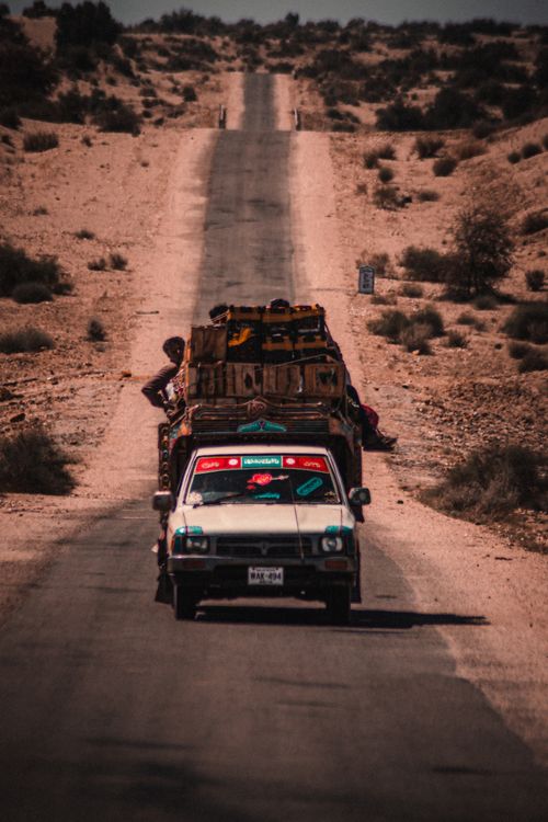 Free A convoy of vehicles travels along a deserted road through a barren desert landscape under the bright sun. Stock Photo
