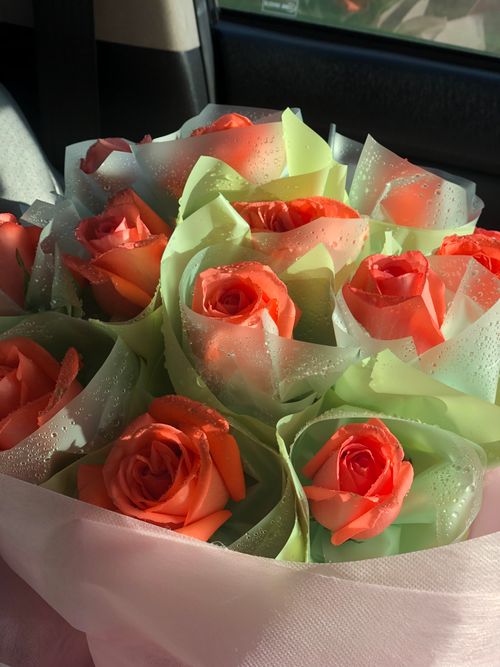 Free A beautiful bouquet of orange roses wrapped in green paper with dewdrops, capturing nature's elegance. Stock Photo