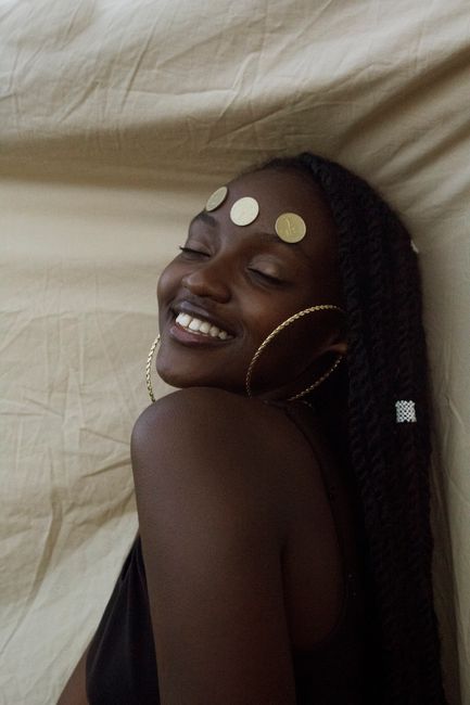 A joyful portrait of a woman with hoop earrings and coins on her forehead, eyes closed.