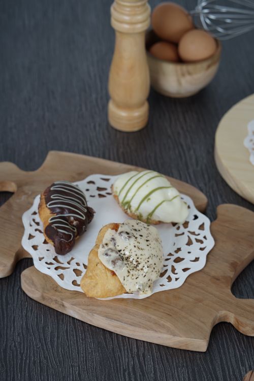 Free Delicious eclairs with chocolate, vanilla, and matcha glaze, elegantly presented on a wooden board. Stock Photo