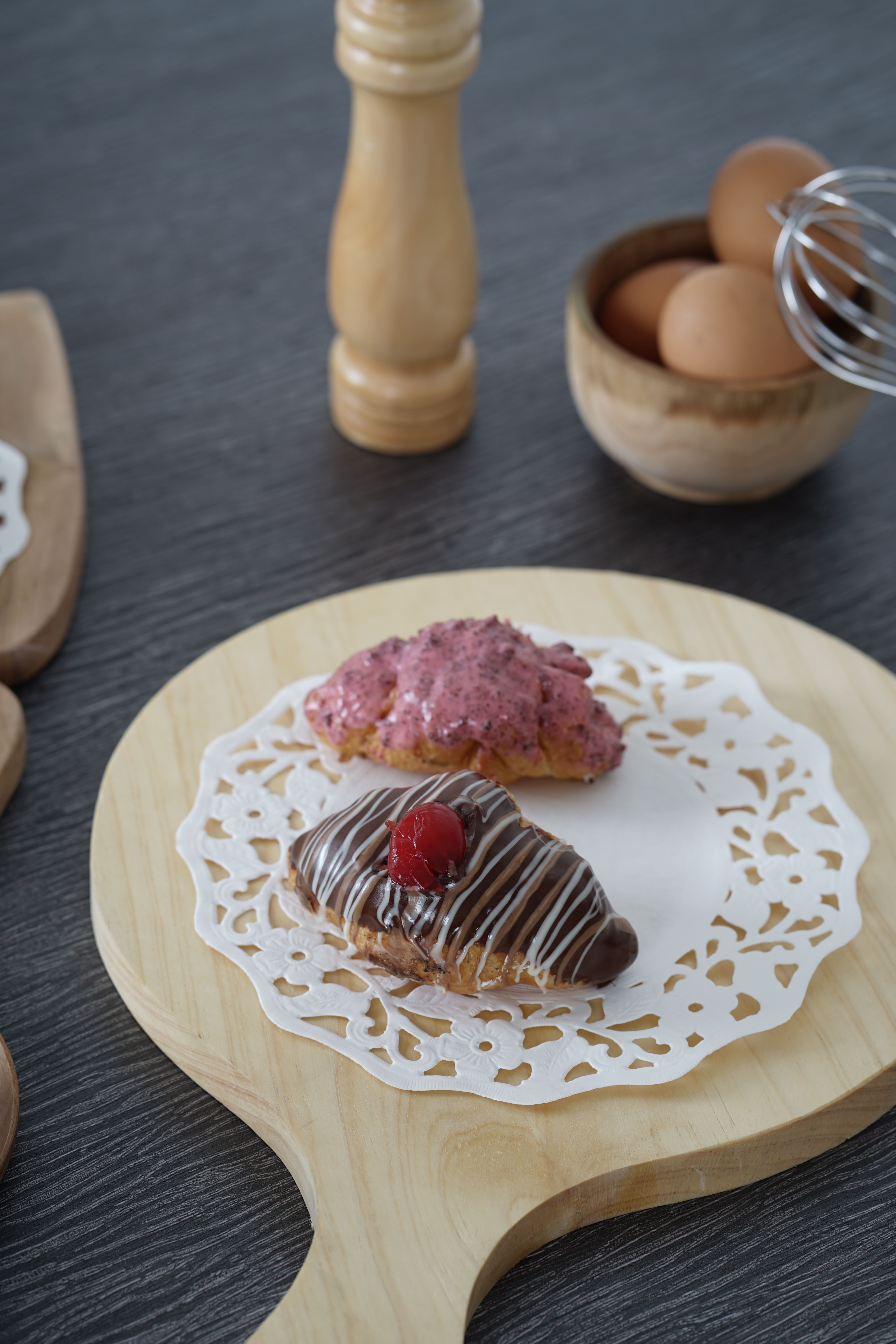 Delicious eclairs topped with chocolate and berries on a wooden board with placed eggs nearby.