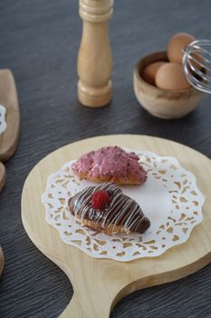 Delicious eclairs topped with chocolate and berries on a wooden board with placed eggs nearby.