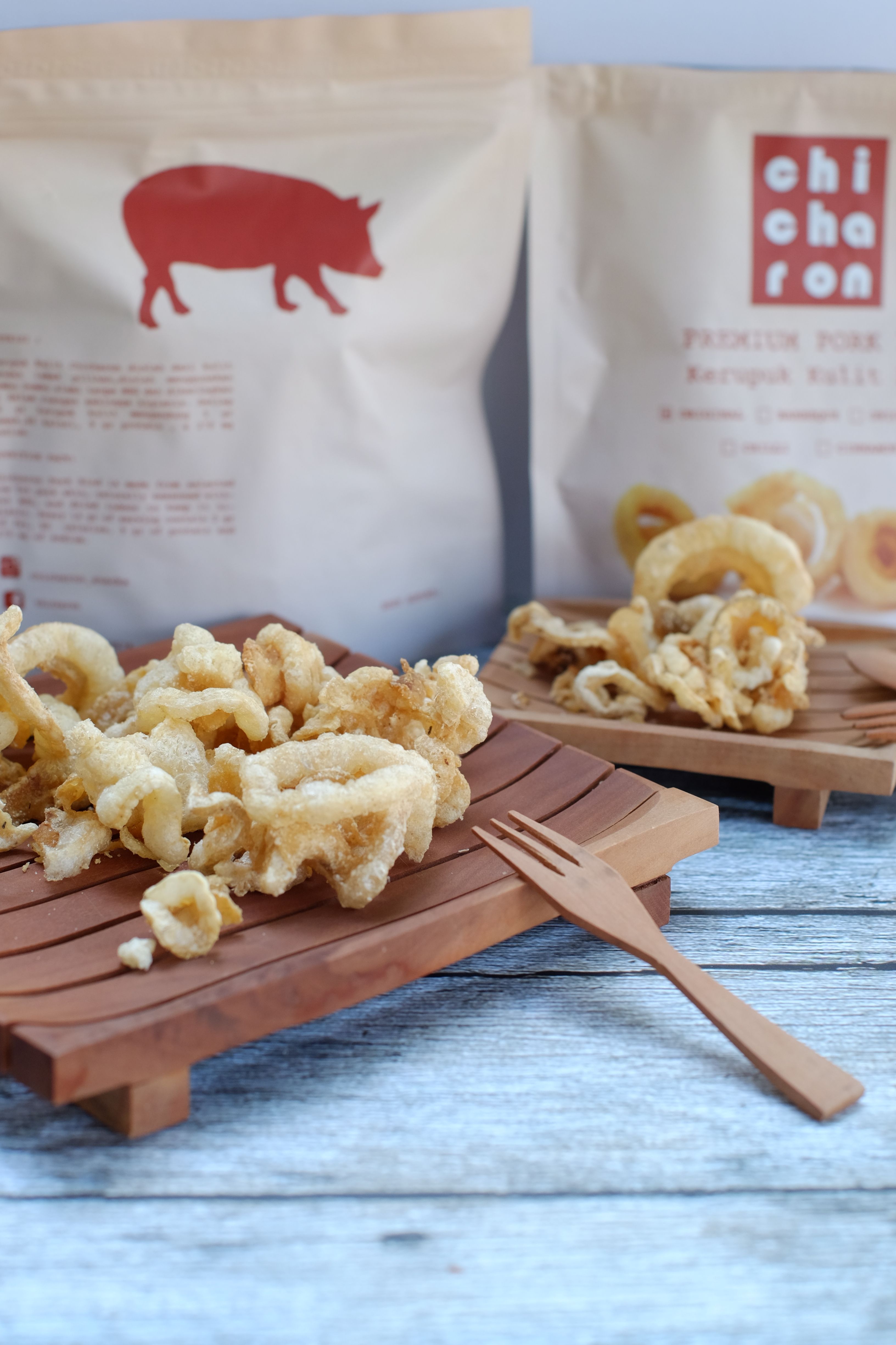 Crispy pork chicharon served on wooden trays with premium packaging in the background.