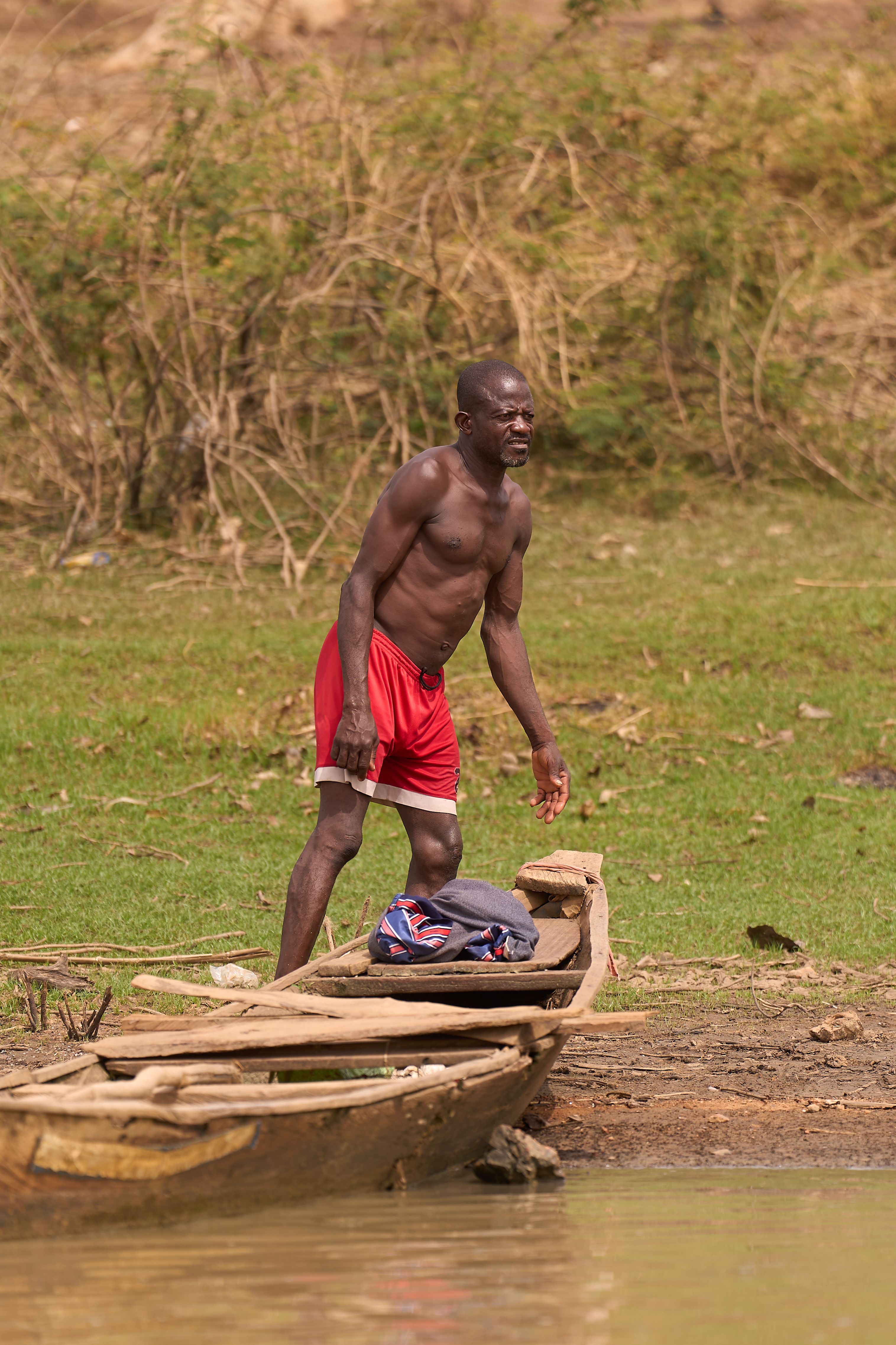 An athletic man standing by the river with a wooden boat in Minna, Nigeria.