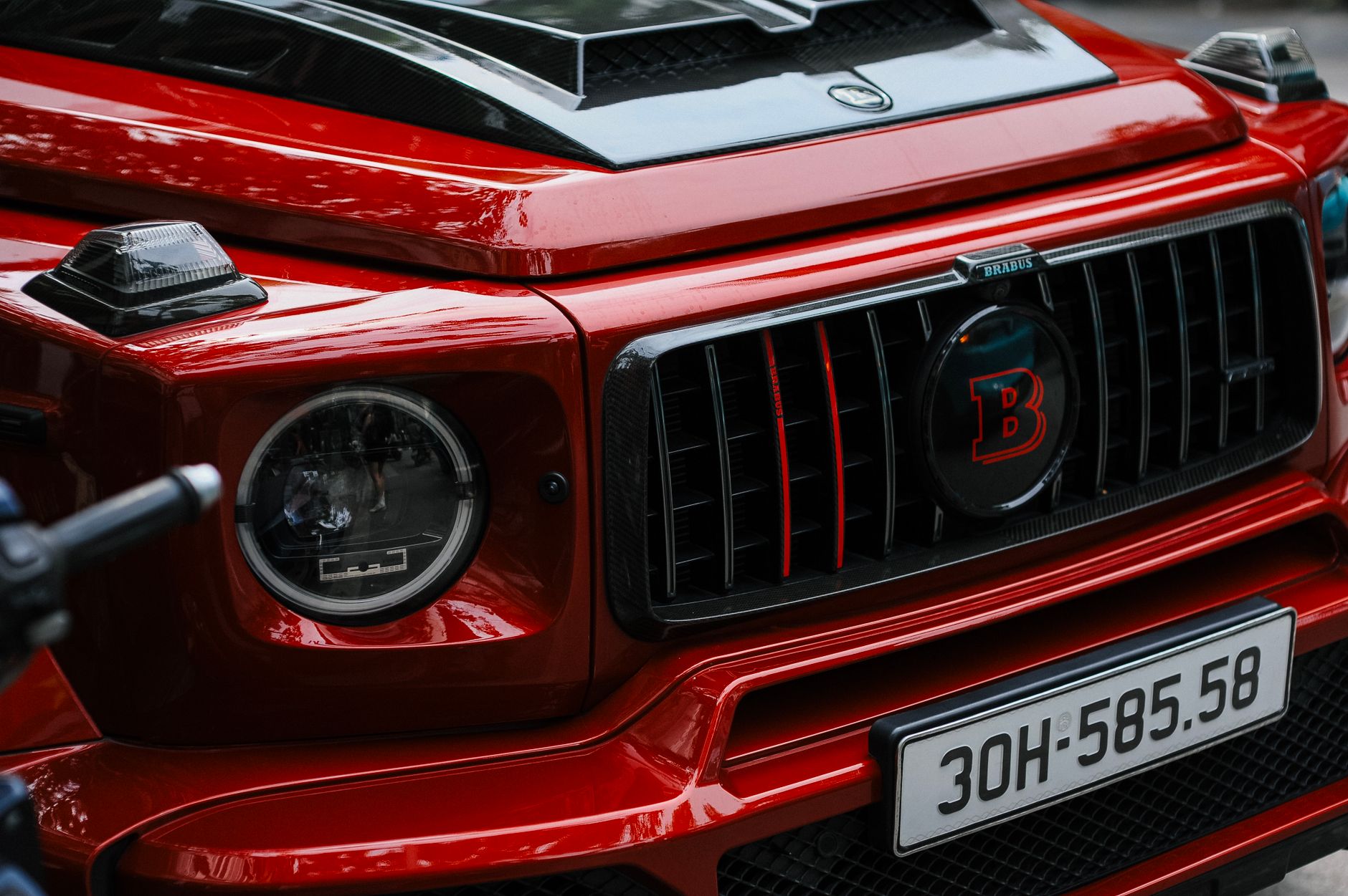 Detailed view of a red luxury car's front grill featuring a custom emblem and headlight design.