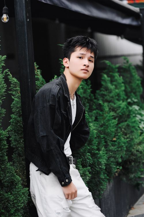 Free Teenager in black denim jacket leans against wall with green backdrop. Stock Photo