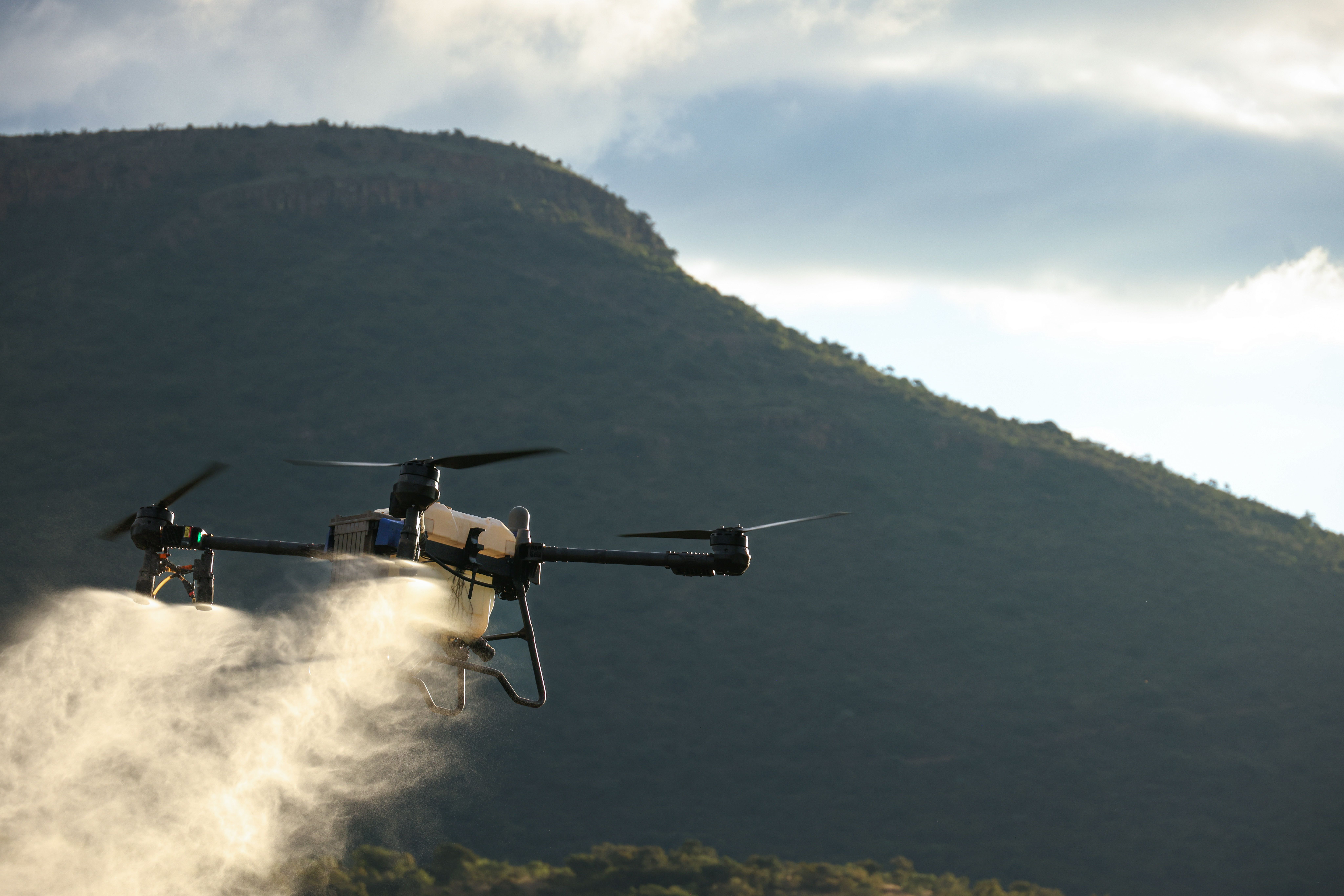 A drone spraying in front of a lush mountain, showcasing modern agricultural technology.