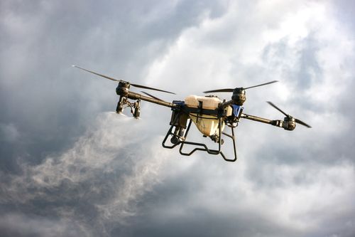 Free A drone dispersing mist in a cloudy sky, showcasing agricultural technology innovation. Stock Photo