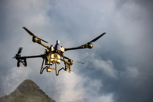 Advanced quadcopter drone soaring in the sky with a dramatic cloud backdrop and mountain scenery.