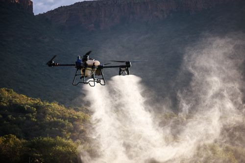 Free A drone actively disperses mist over a lush, mountainous area during twilight, highlighting modern agricultural technology. Stock Photo