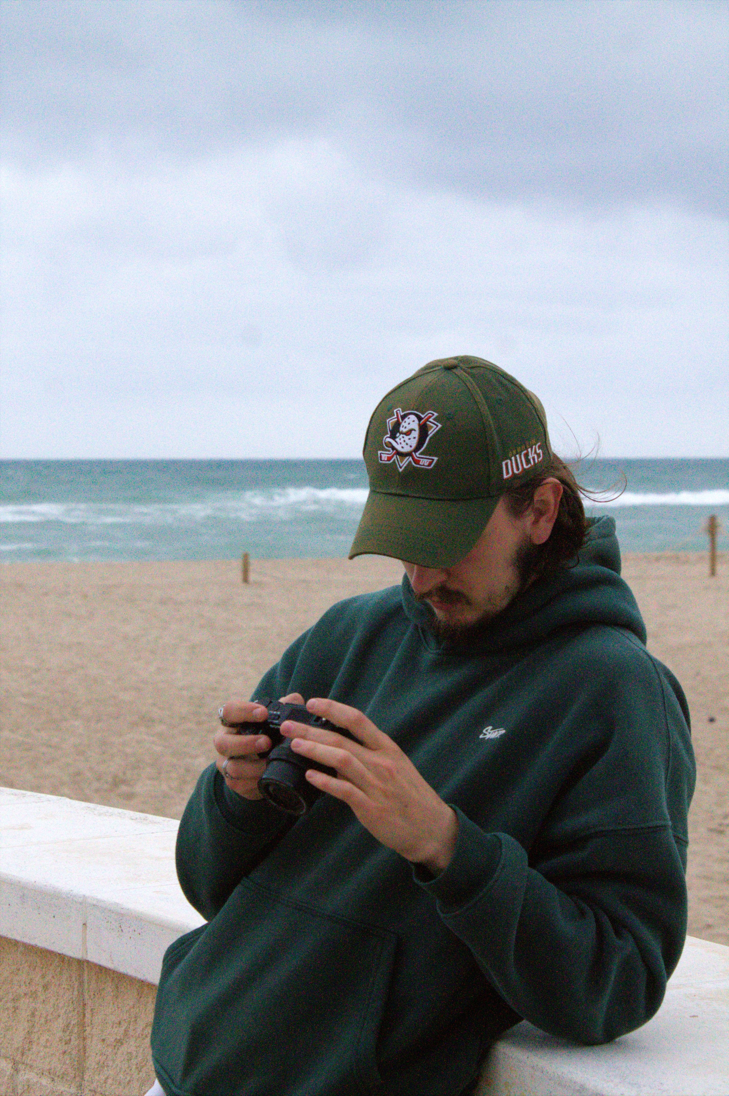 Casual scene of a man in a hoodie taking photos at a cloudy beach.